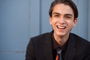 Professional headshot against a blue wall wearing a dark suit and red tie.