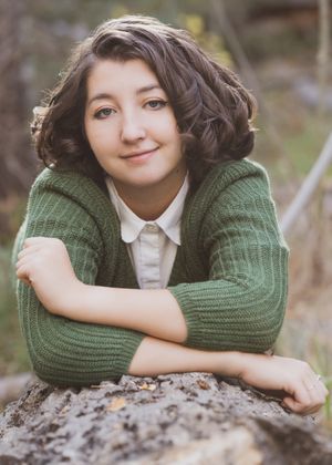A person in a green sweater poses casually while resting on rocks outdoors.