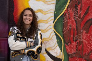 Casual pose against vibrant street art mural wearing varsity jacket.