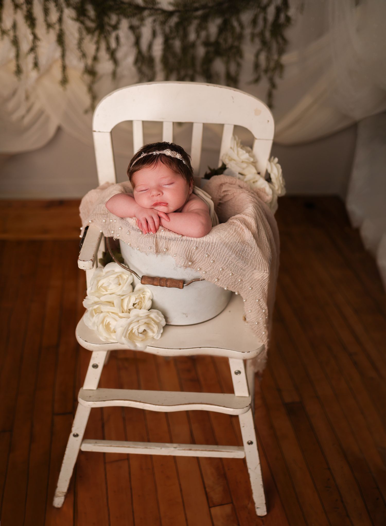 Newborn photography on vintage white chair with lace and floral accents.