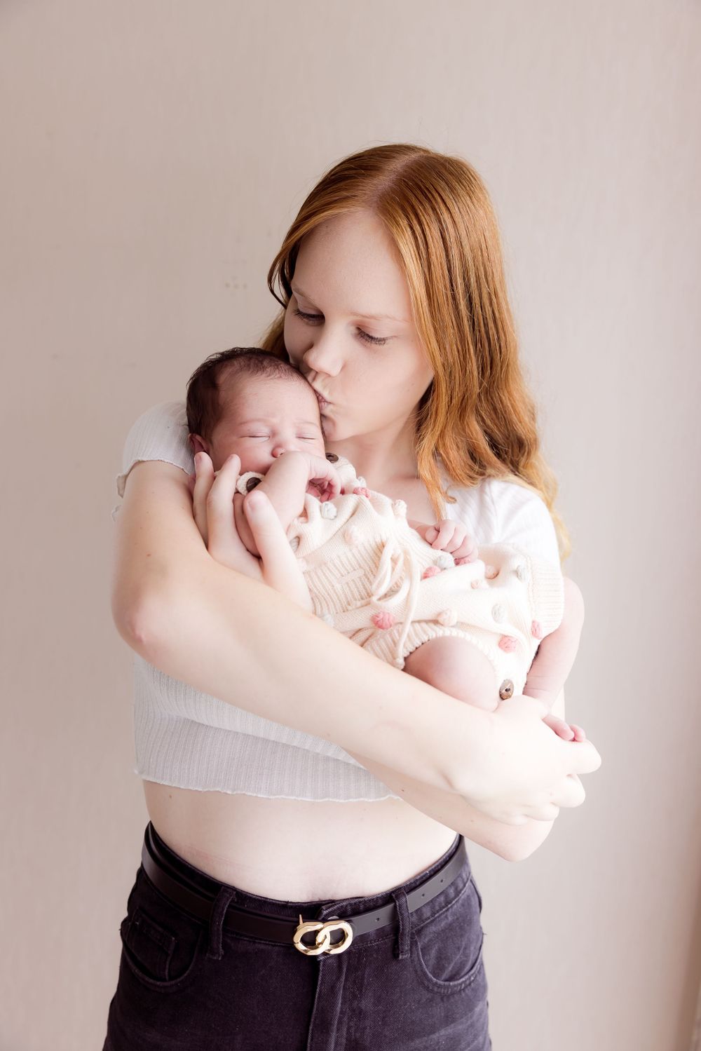 lady with long red hair holding baby and kissing baby forehead