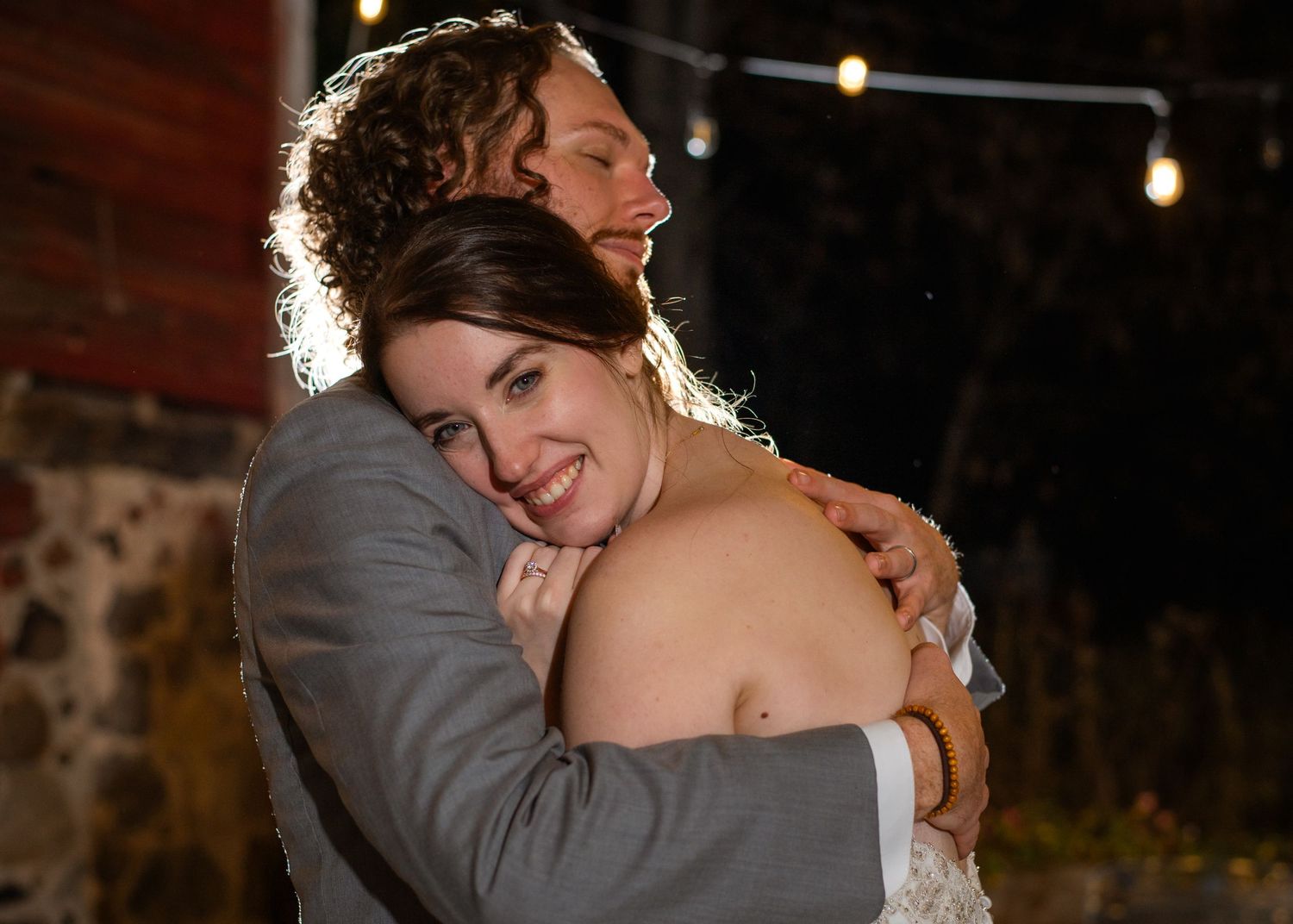 Romantic evening portrait of newlyweds embracing with string lights in background.