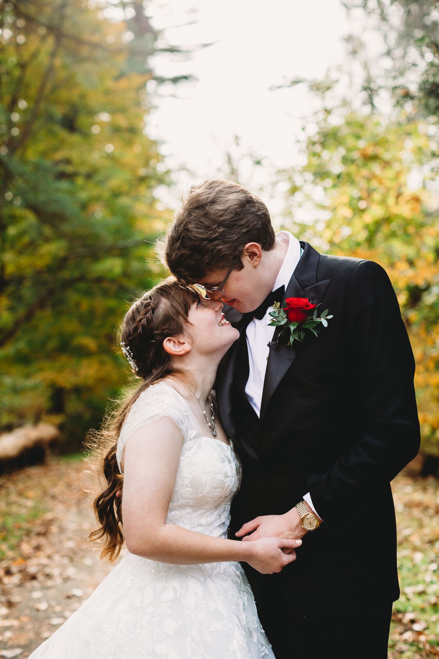 a wedding couple poses with their faces close together, smiling lovingly; it is golden hour and the forest is glowing