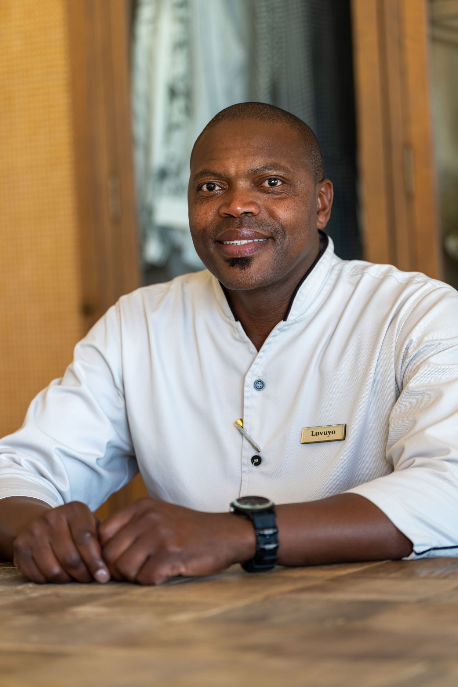 Restaurant staff member in white chef coat seated at wooden table.