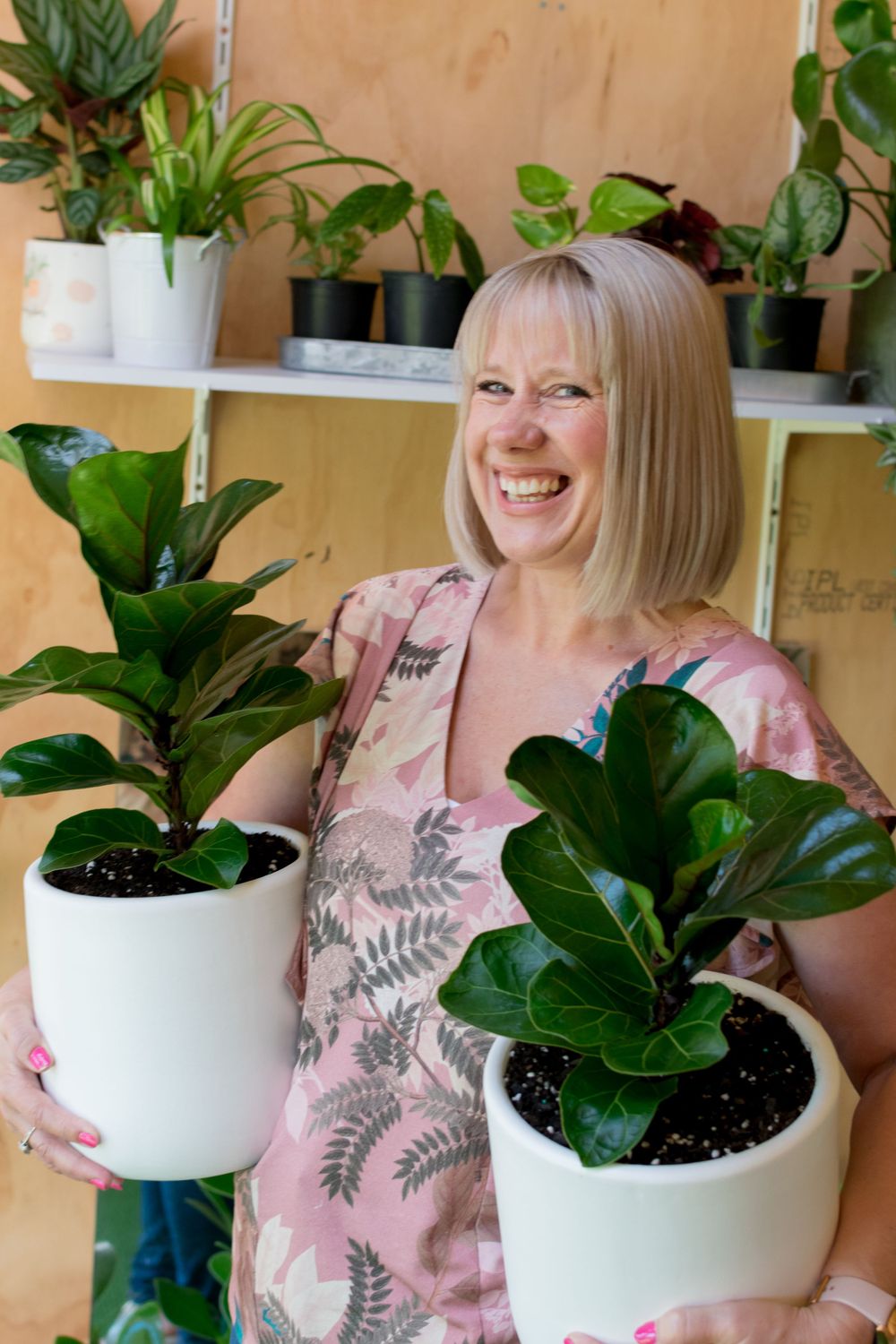 Online plant shop owner Chontelle holds a large potted plant under each arm as she smiles at the photographer