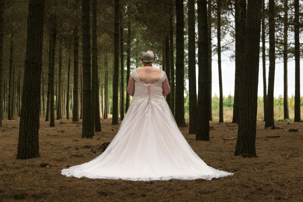On location portrait of a bride in a forest facing away from the camera with the train of her gown spread behind