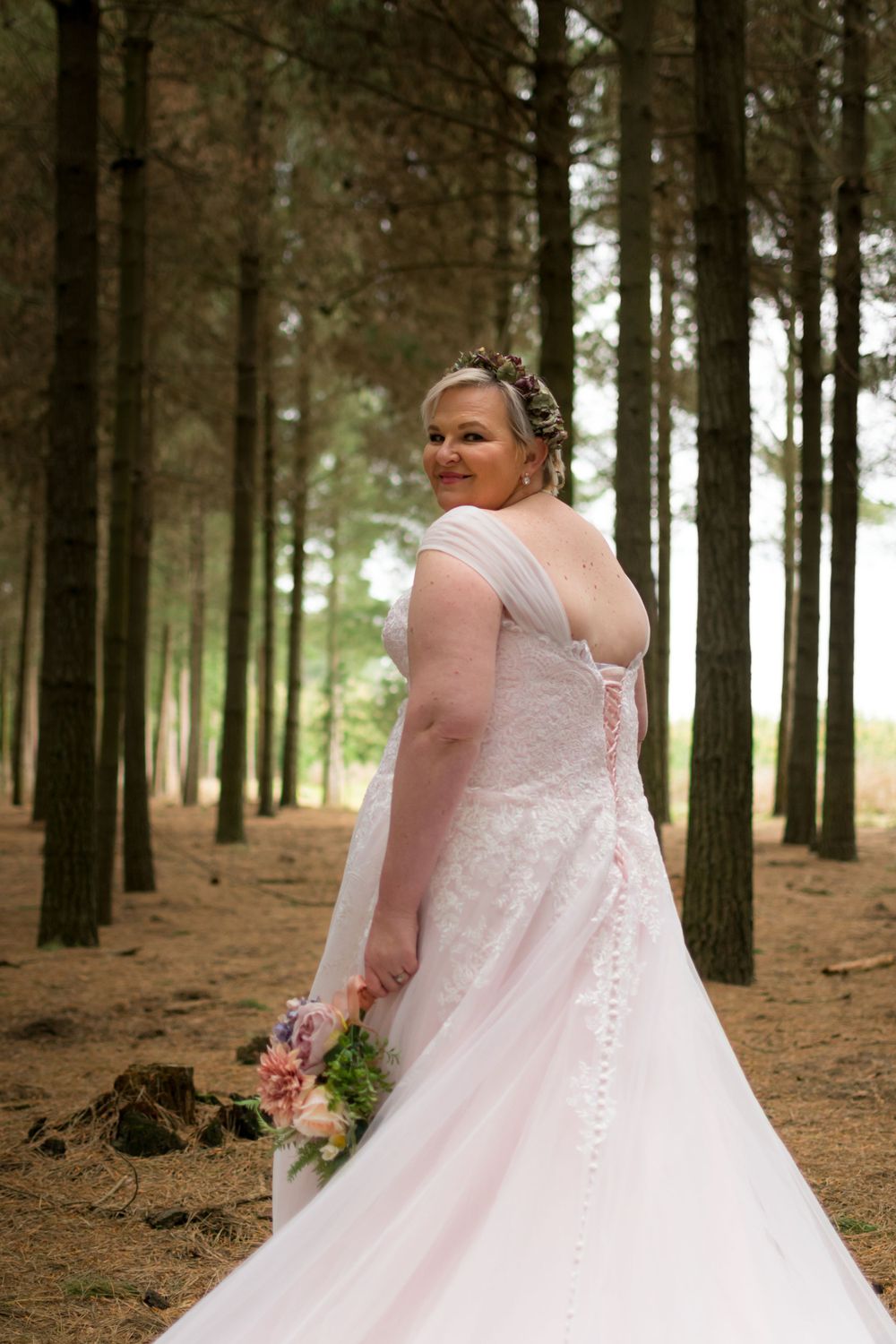 Portrait of a bride looking over her shoulder towards the camera while standing in a forest