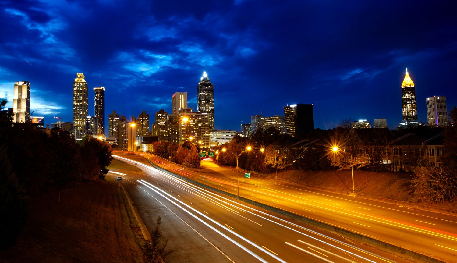 Atlanta skyline at night with light trails from traffic on highway in the foreground.