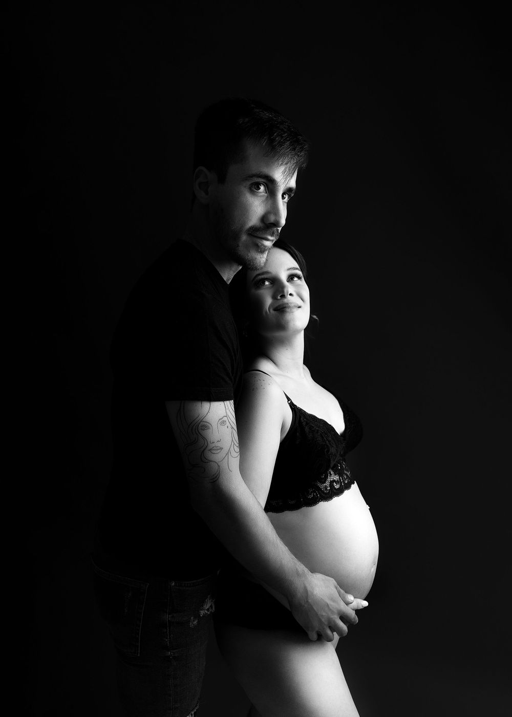 Dramatic black and white maternity portrait against dark background.
