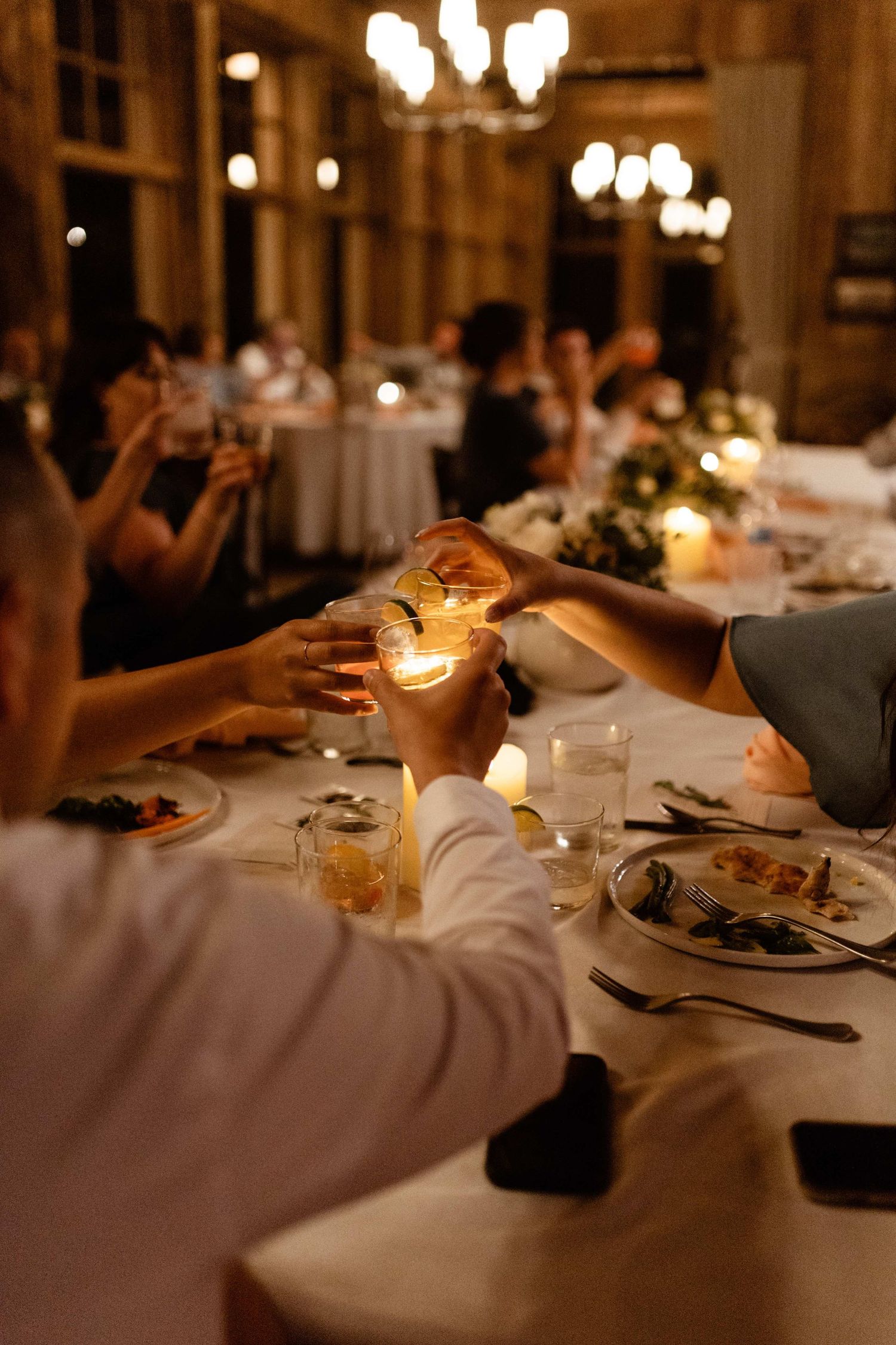 Candlelit wedding reception dinner with guests reaching for glowing candles on elegant table settings.