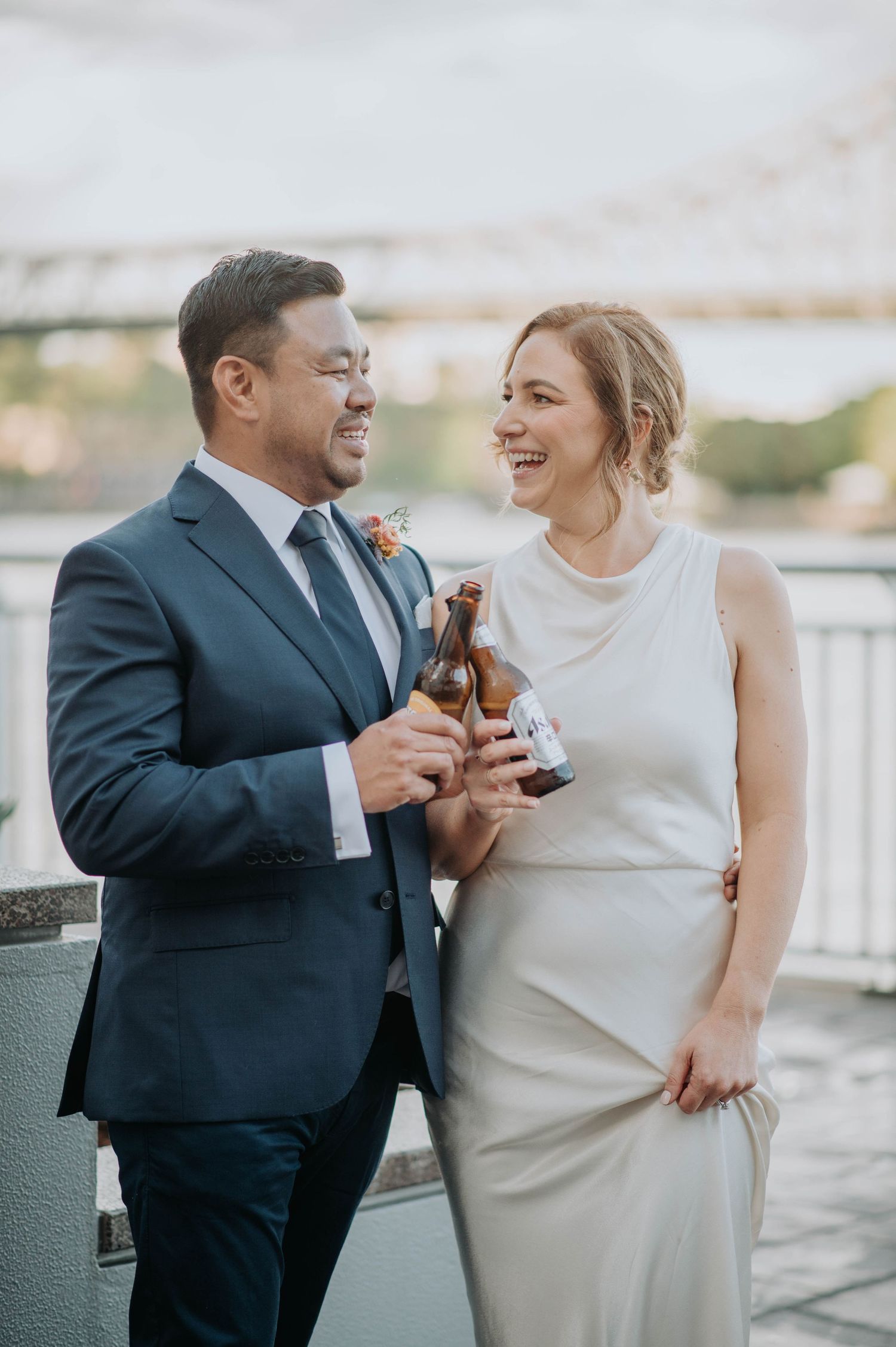 A couple shares drinks and laughter during their wedding celebration on an outdoor terrace.
