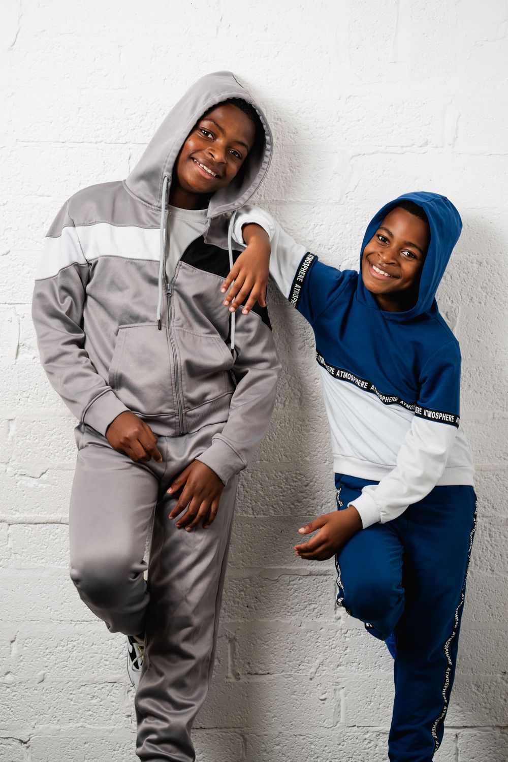 Two youth in coordinating hooded sweatsuit sets posing against white wall in Guildford, Surrey.