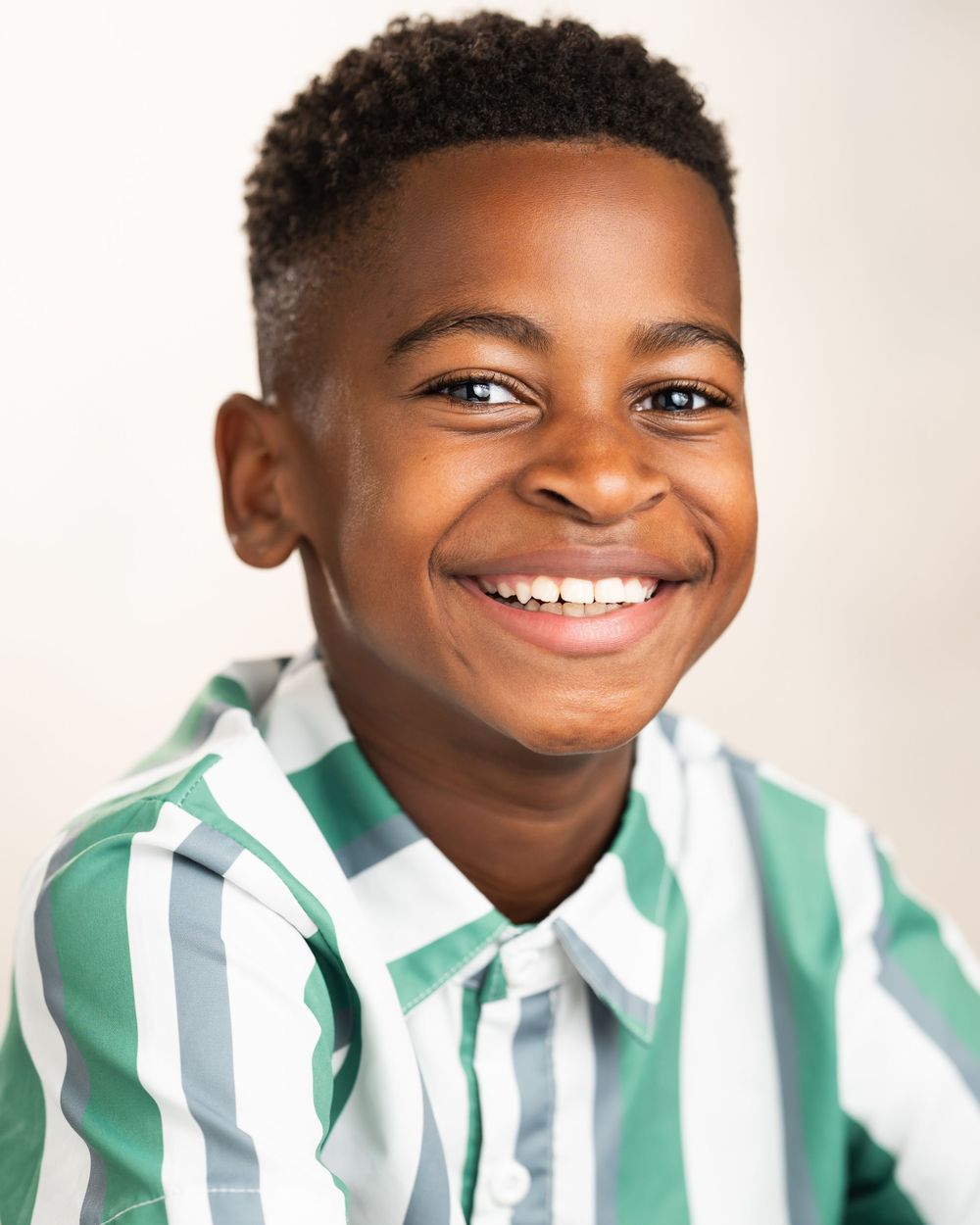 Portrait of youth wearing striped green and white collared shirt against light background in Guildford, Surrey.