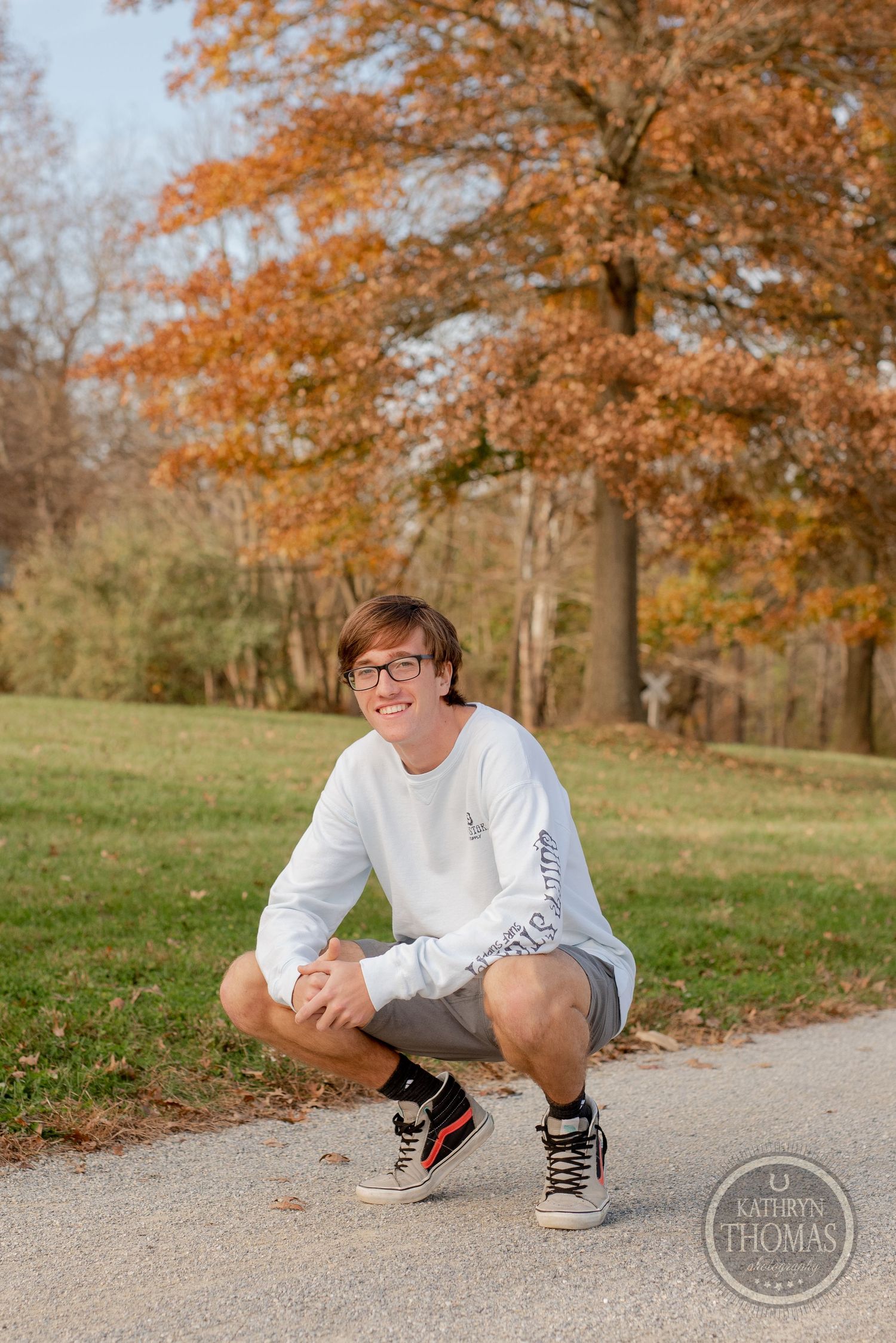 Student crouches on path surrounded by fall trees wearing athletic casual wear.