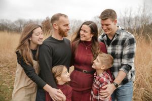 Family embracing in tall grass field during autumn sunset photo session.