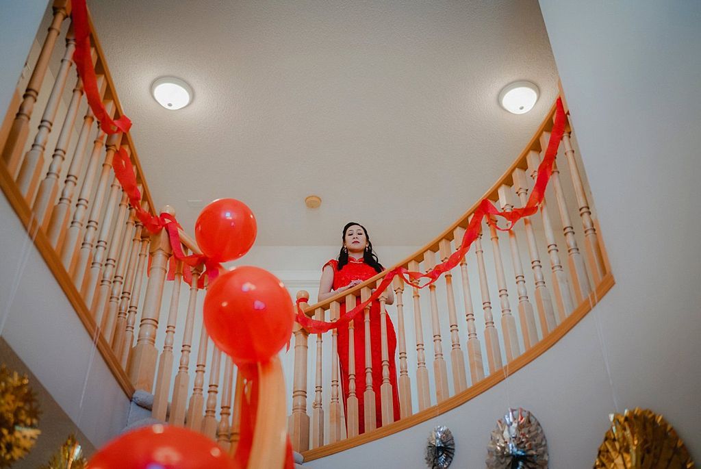 Red dress against wooden staircase decorated with matching balloons and streamers.