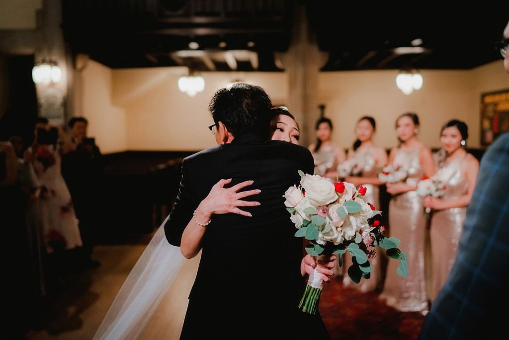 Emotional embrace during wedding ceremony with bridesmaids in pink dresses watching.