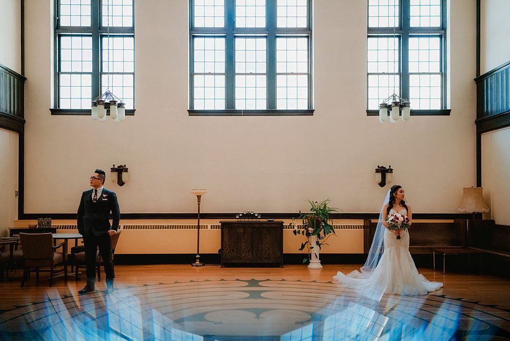 Elegant wedding ceremony in a grand room with tall windows and polished wooden floors.