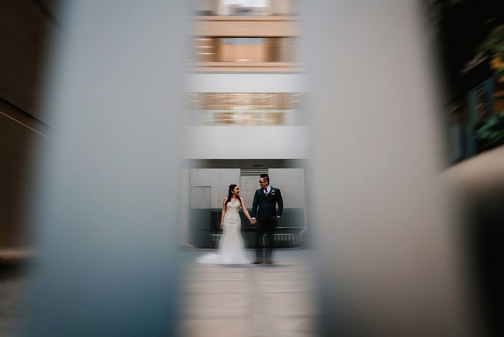 Framed wedding couple through architectural elements creating depth and perspective.