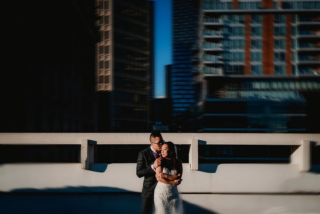 Urban rooftop wedding portrait at sunset with city buildings in background.
