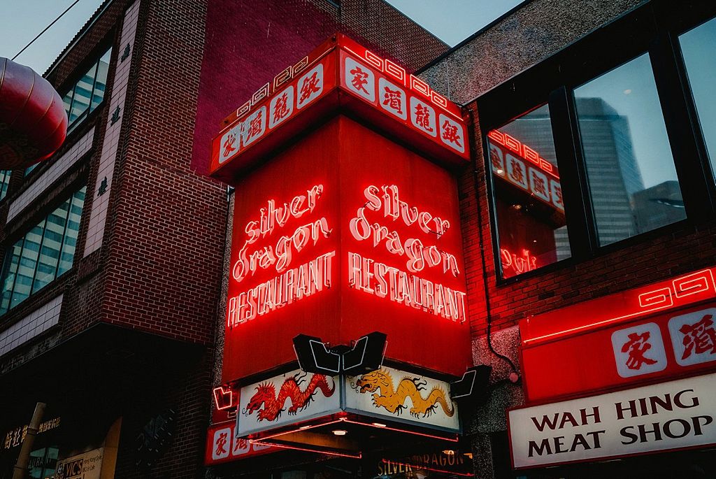 Red neon signs illuminate a storefront in an Asian restaurant district at night.