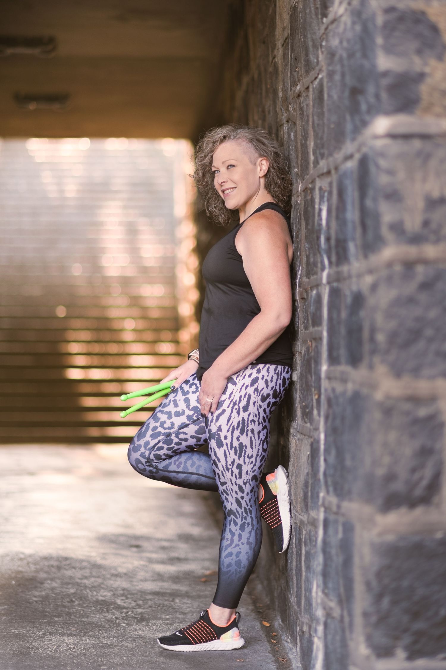 Fitness instructor leaning against stone wall in tunnel with one leg rested on wall smiling looking away