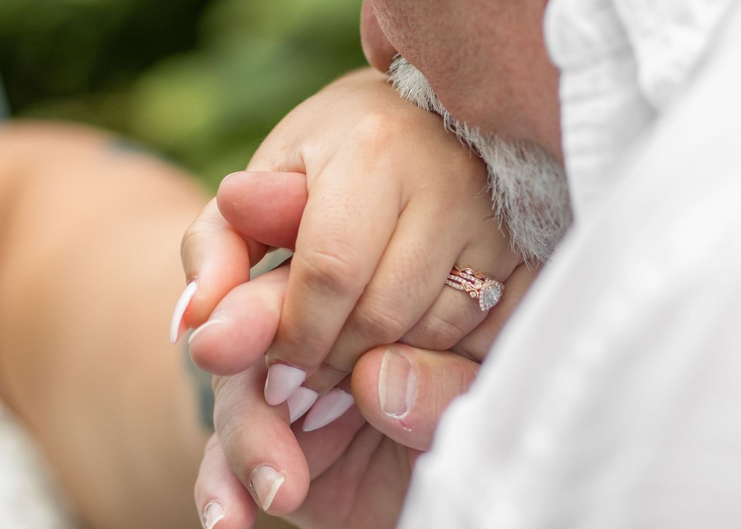 Close-up photo of newlyweds holding hands with wedding rings visible against a soft blurred background.