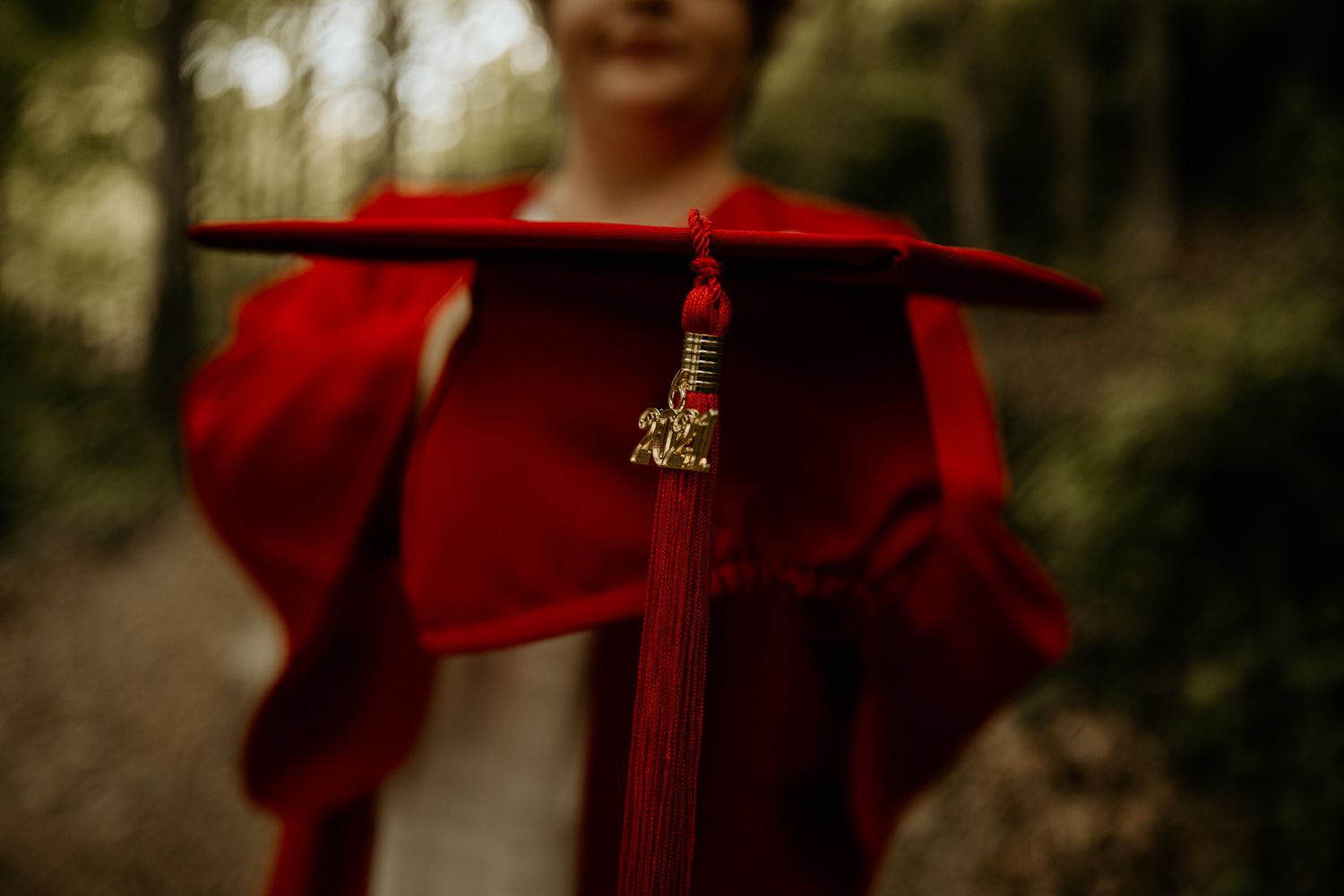 A bright red graduation cap and tassel shown in detail against a blurred natural background.