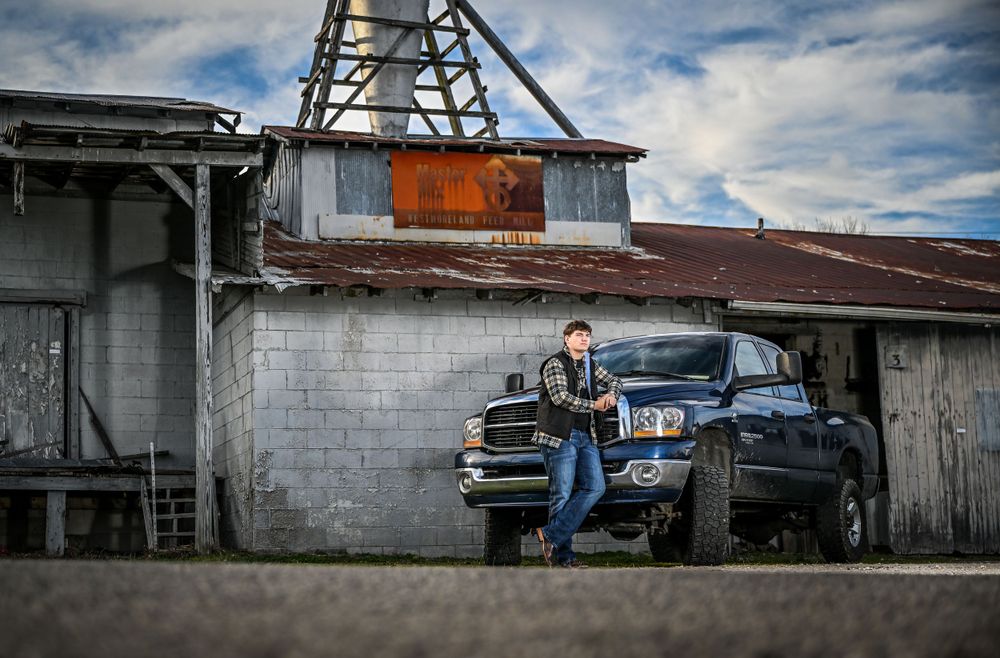 A rustic industrial setting with a pickup truck parked next to a weathered building with metal roofing.