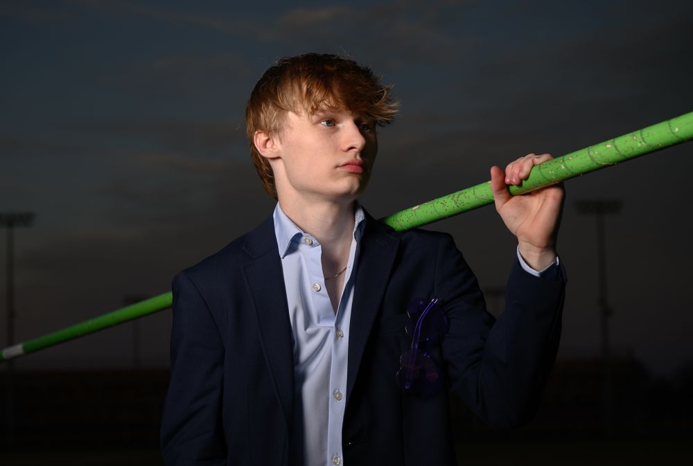 Dramatic portrait with person holding green pole wearing business attire in evening light.