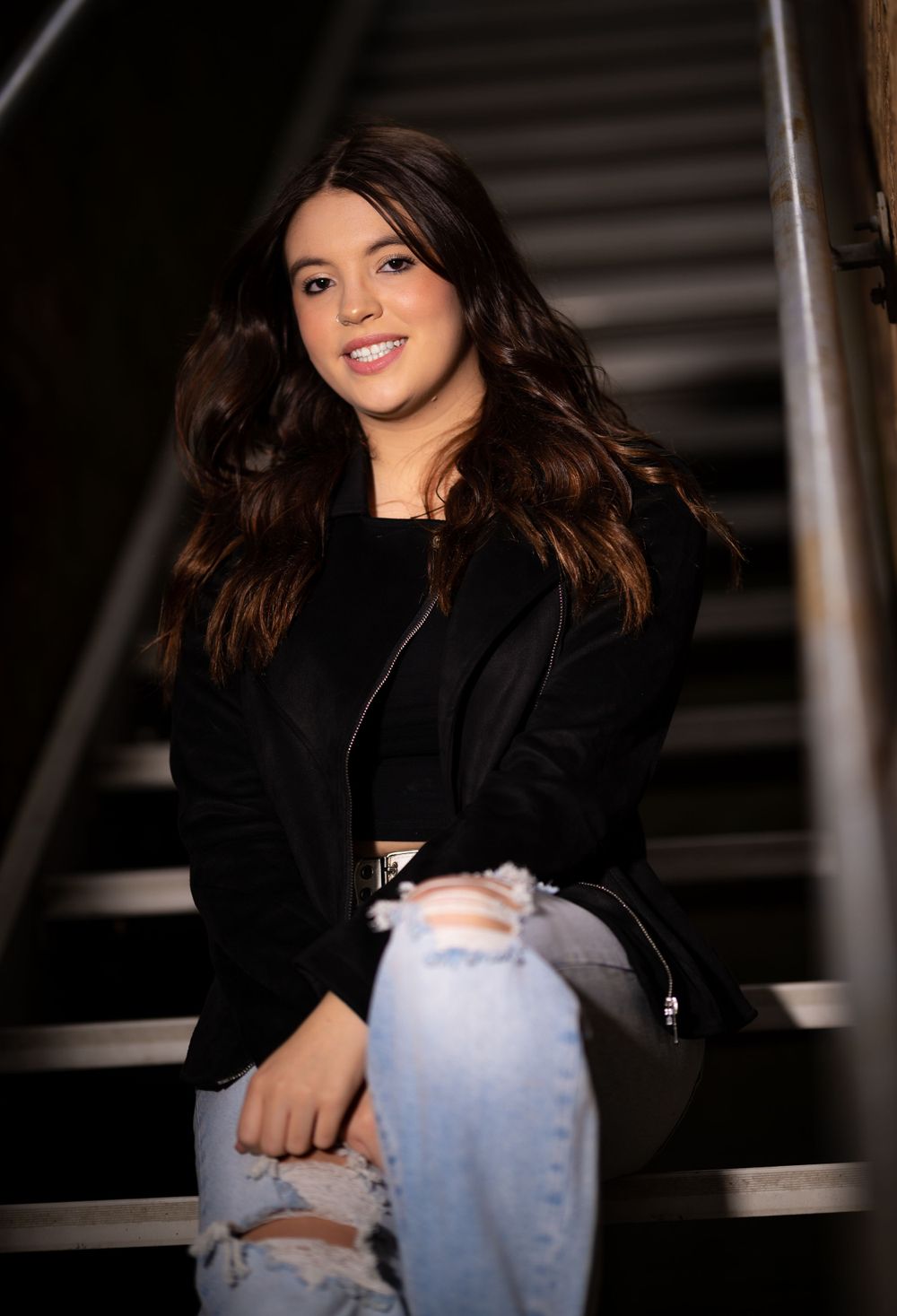 Portrait on industrial staircase of person wearing black jacket and distressed denim.