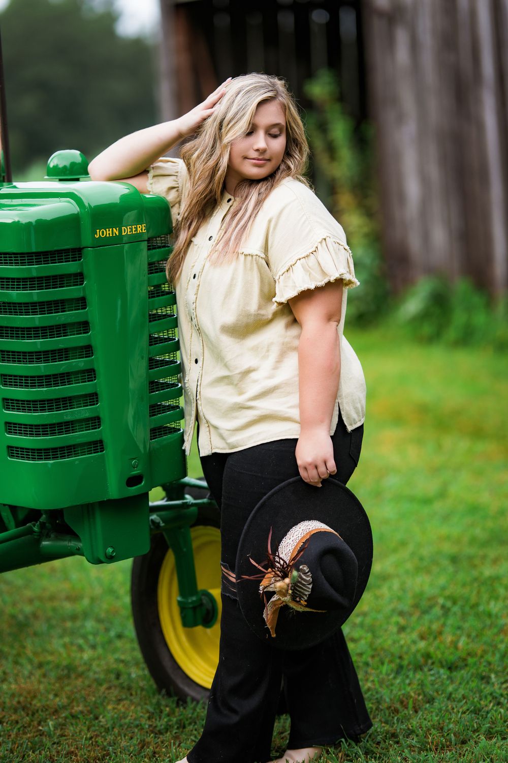 Senior portrait with vintage John Deere tractor in rustic farm setting.