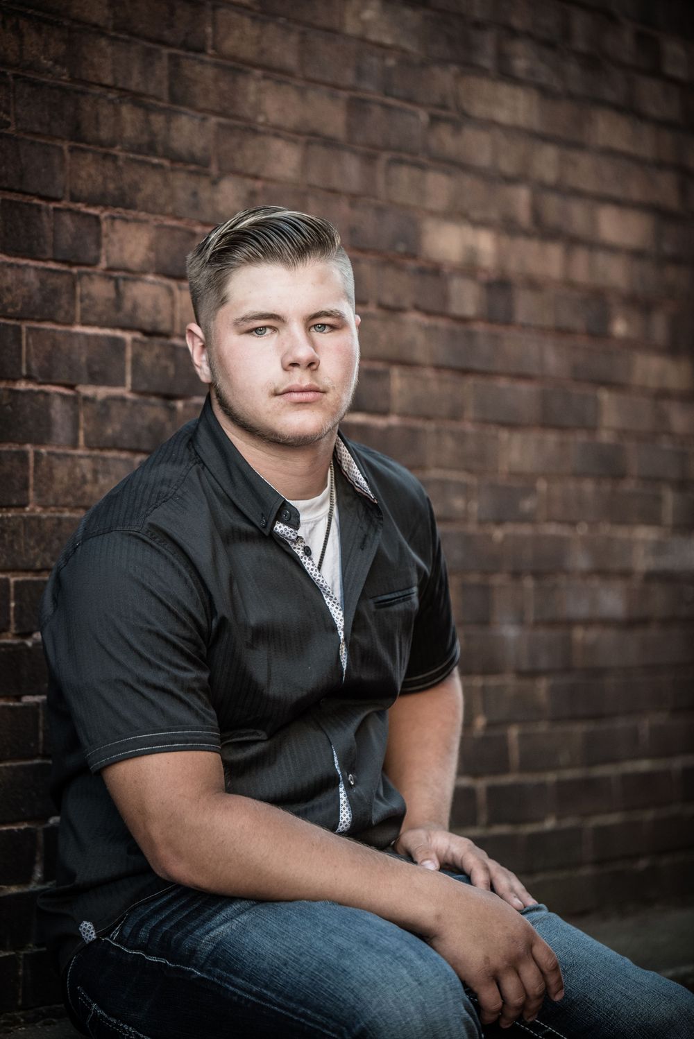 Senior guy sitting beside a brick wall