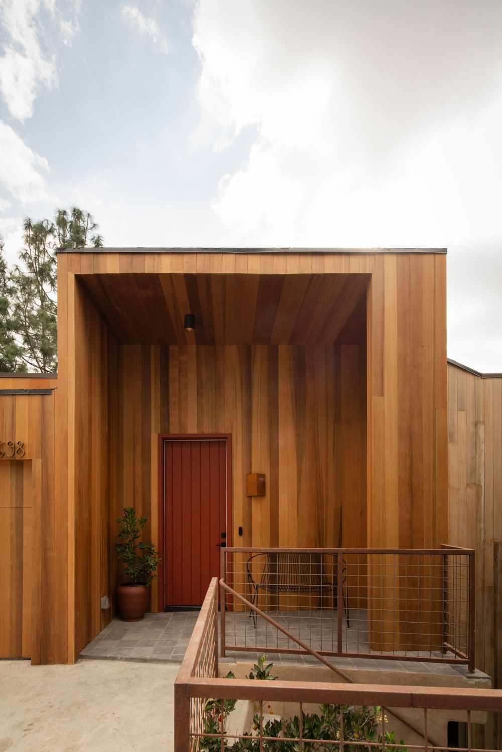 Modern cedar-clad entryway with red door and metal railing detail.