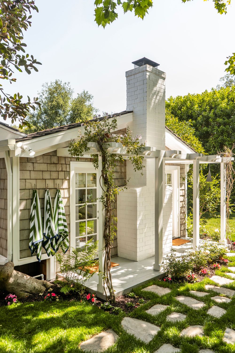 Charming cottage exterior with white trim, climbing vines, and stone pathway through flowering garden.