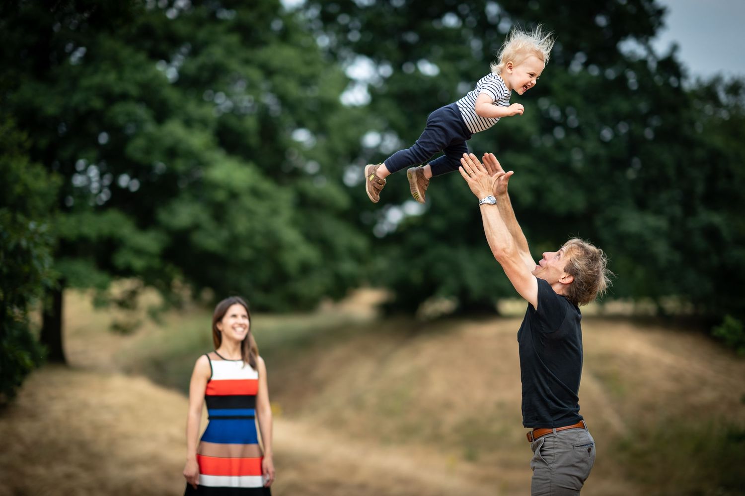 Father throw toddler in the air on the edge of Greenwich Park