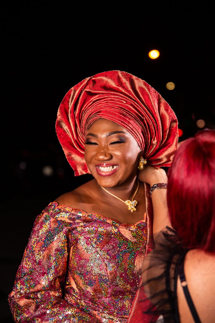 Person wearing vibrant red headwrap and sparkly formal dress smiling during nighttime celebration.