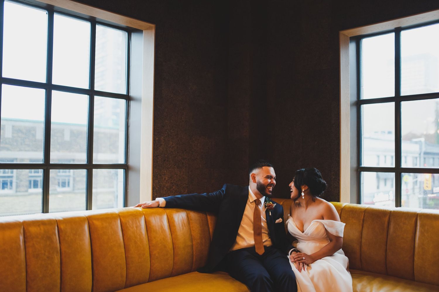 Couple sitting together on orange leather booth seating by windows.