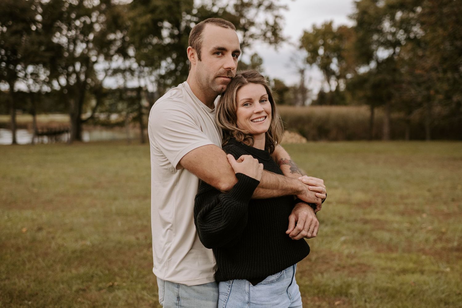 Couple shares an intimate embrace while standing in a golden grass field at sunset.