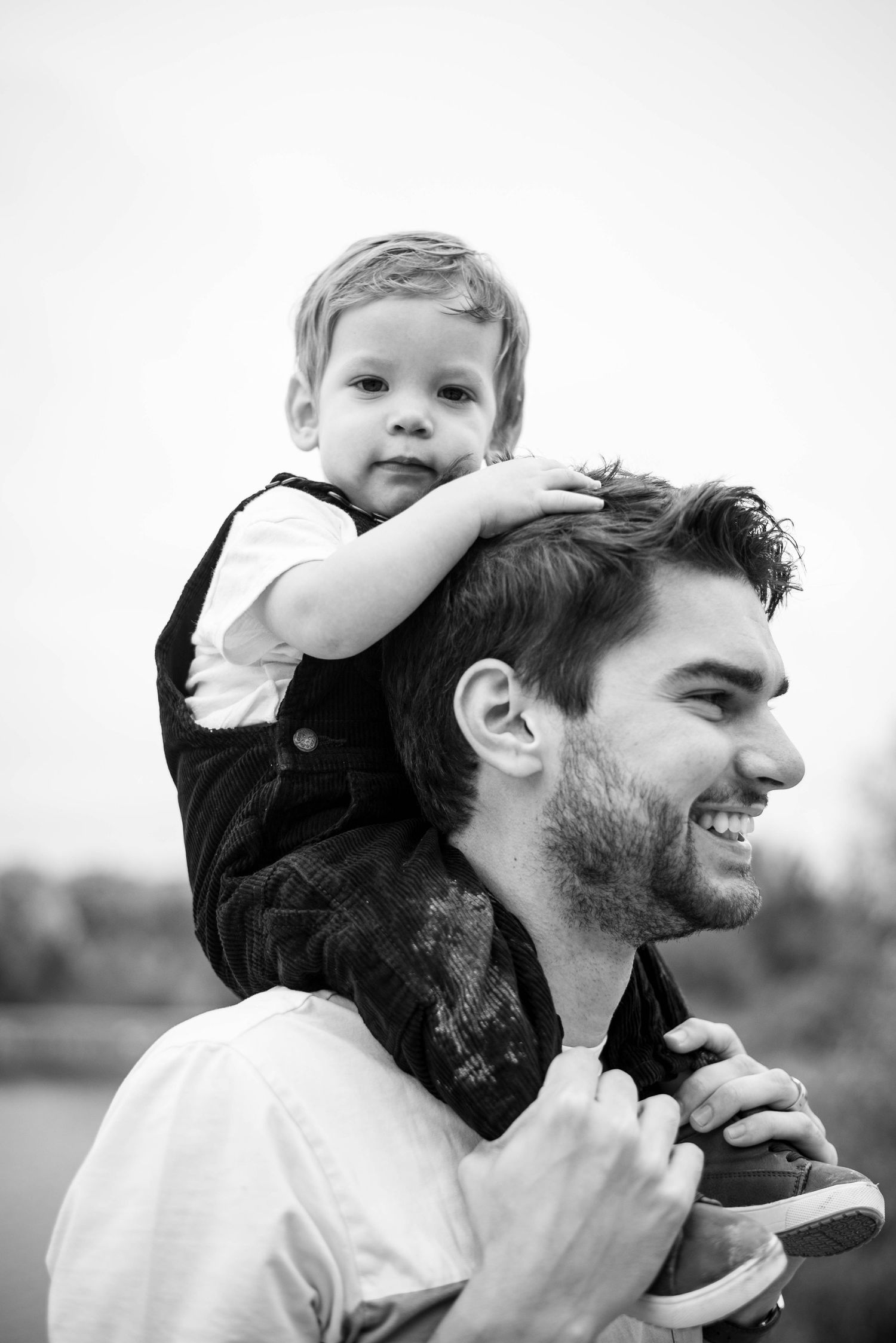 Black and white portrait of a little boy on his dad's shoulders.