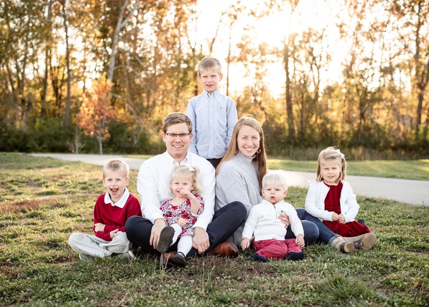A picture of a family of seven sitting in front of the sunset by St. Louis Photographer Isabel Nolan.