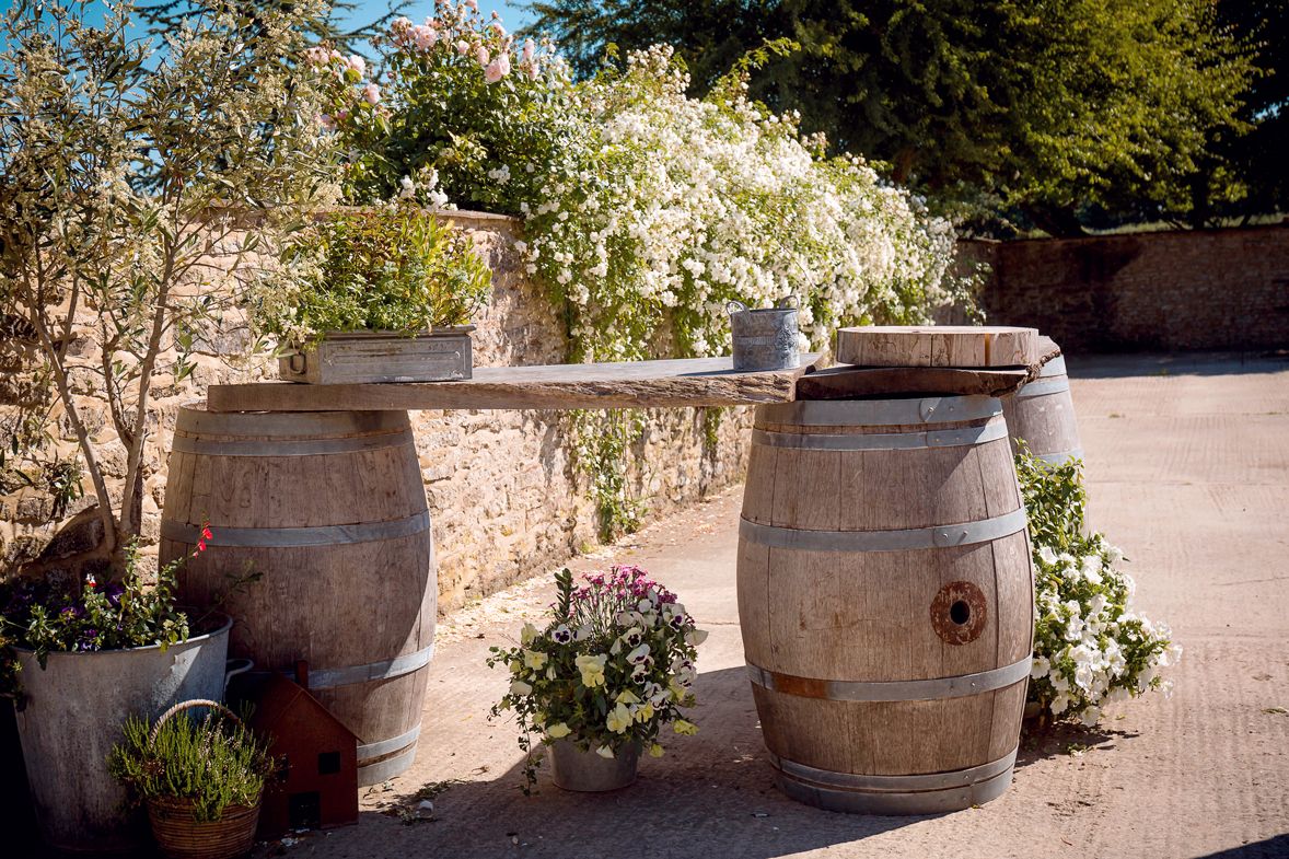 Rustic wine barrel table arrangement decorated with white flowers in a garden setting.