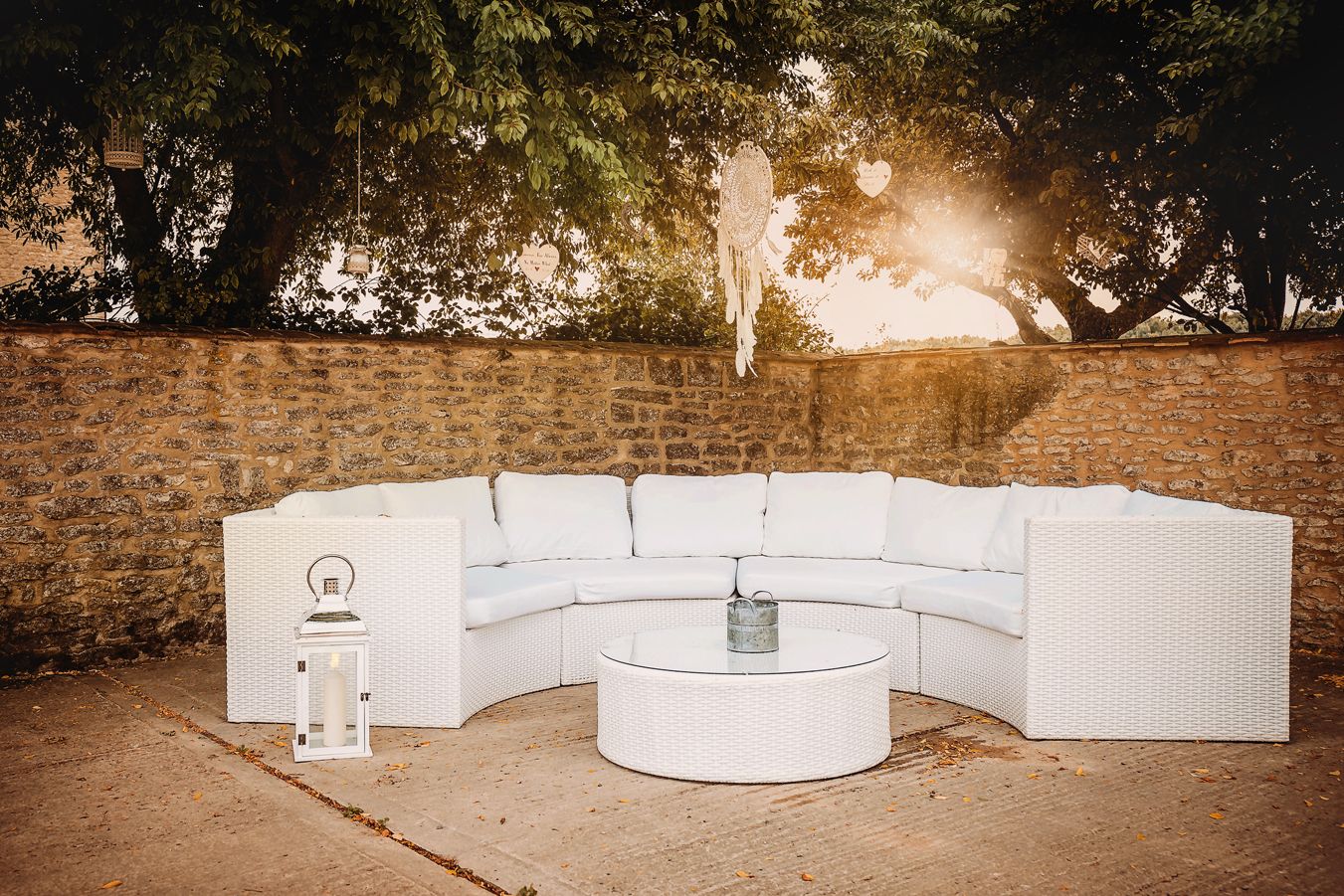 Modern white curved outdoor lounge seating arrangement against a stone wall at sunset.