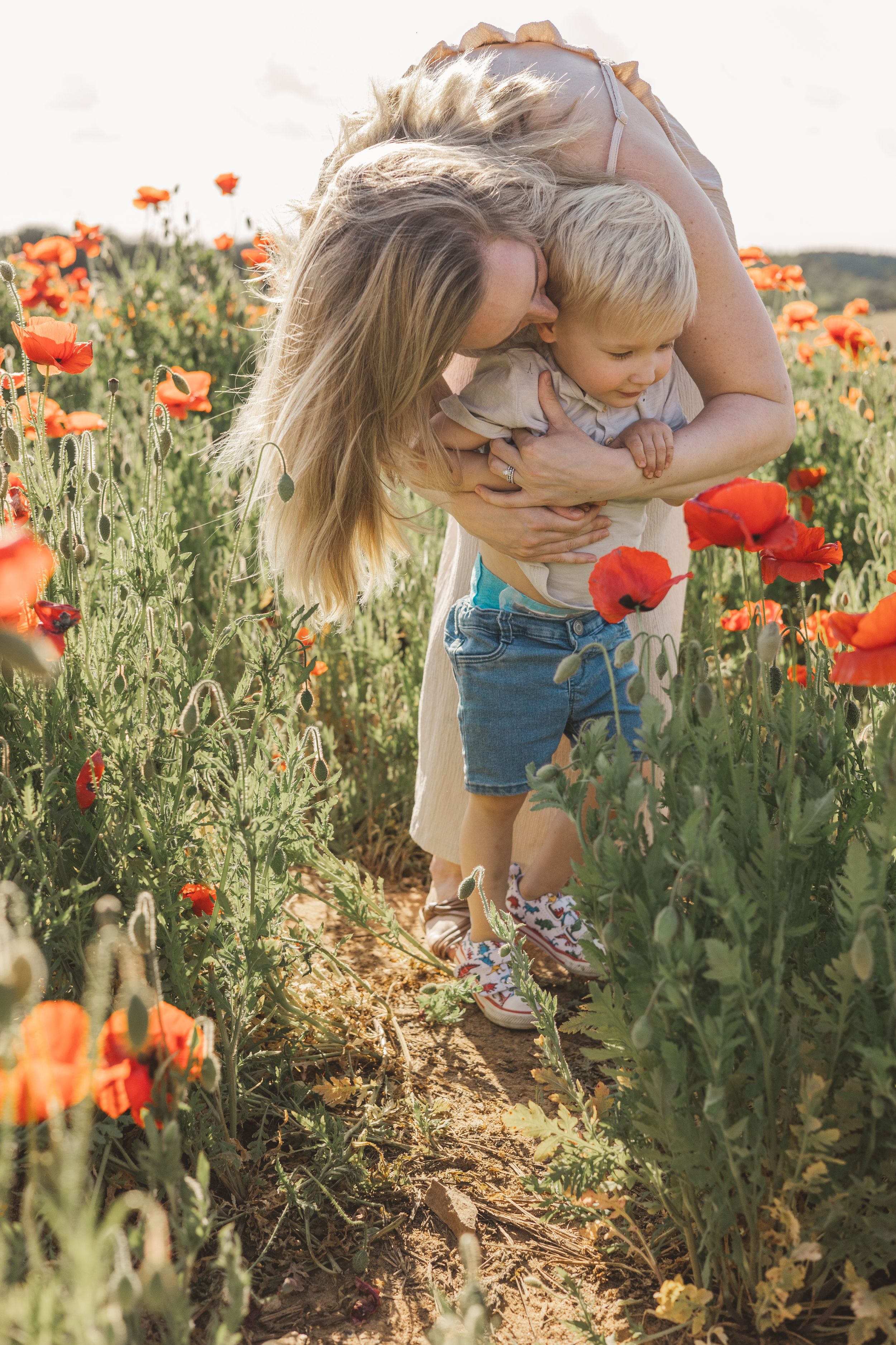 Mother hugging and kissing young toddler child in a stunning red poppy flower field.
