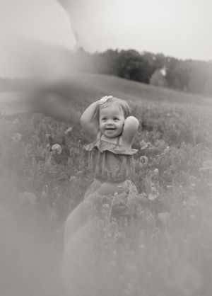 Happy baby girl in floral romper smiling in wildflower meadow, dreamy vintage black and white portrait.
