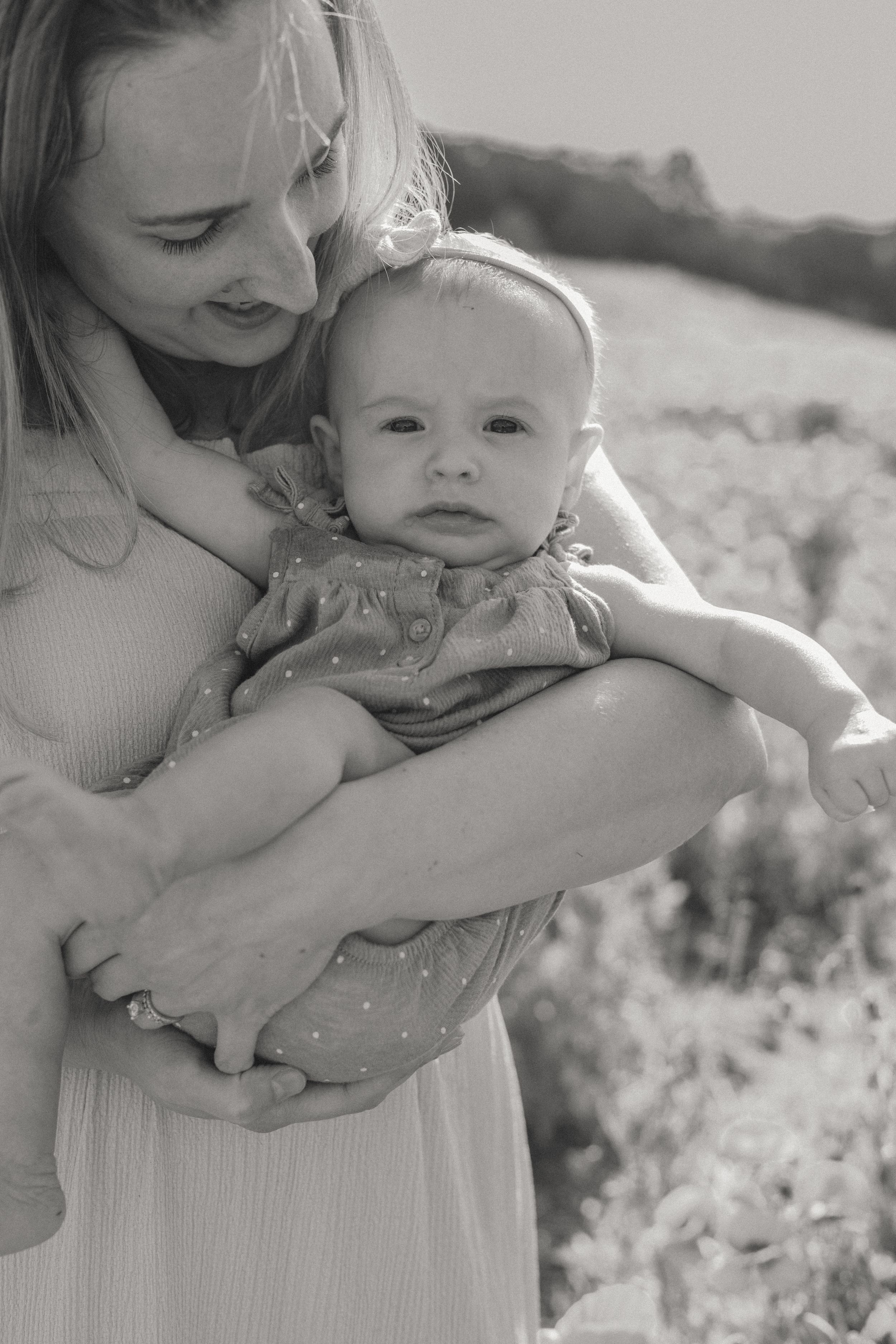 Black and white portrait of mother tenderly cradling newborn baby outdoors in nature.