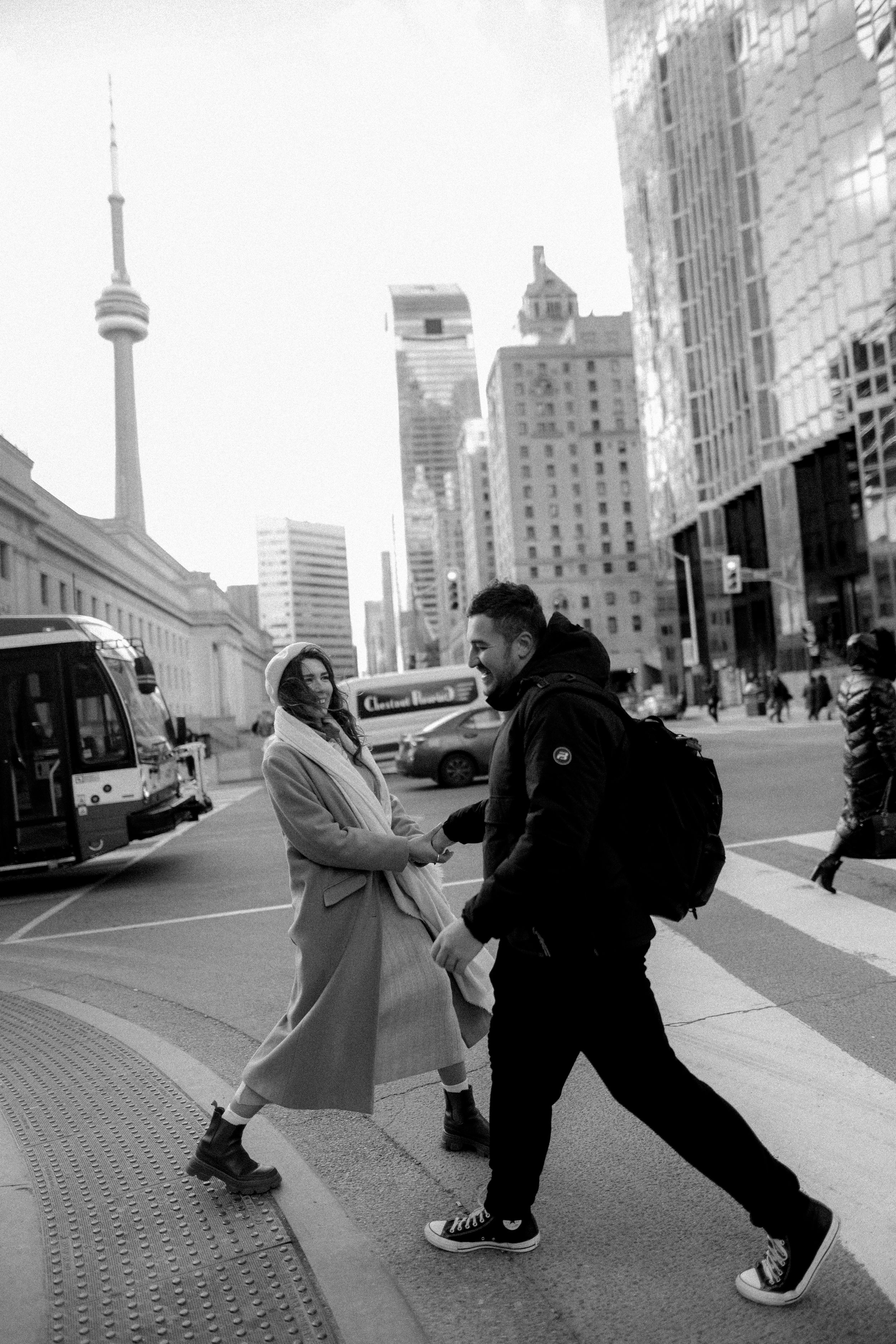 A couple playfully poses on a Toronto street with the CN Tower visible in the background.
