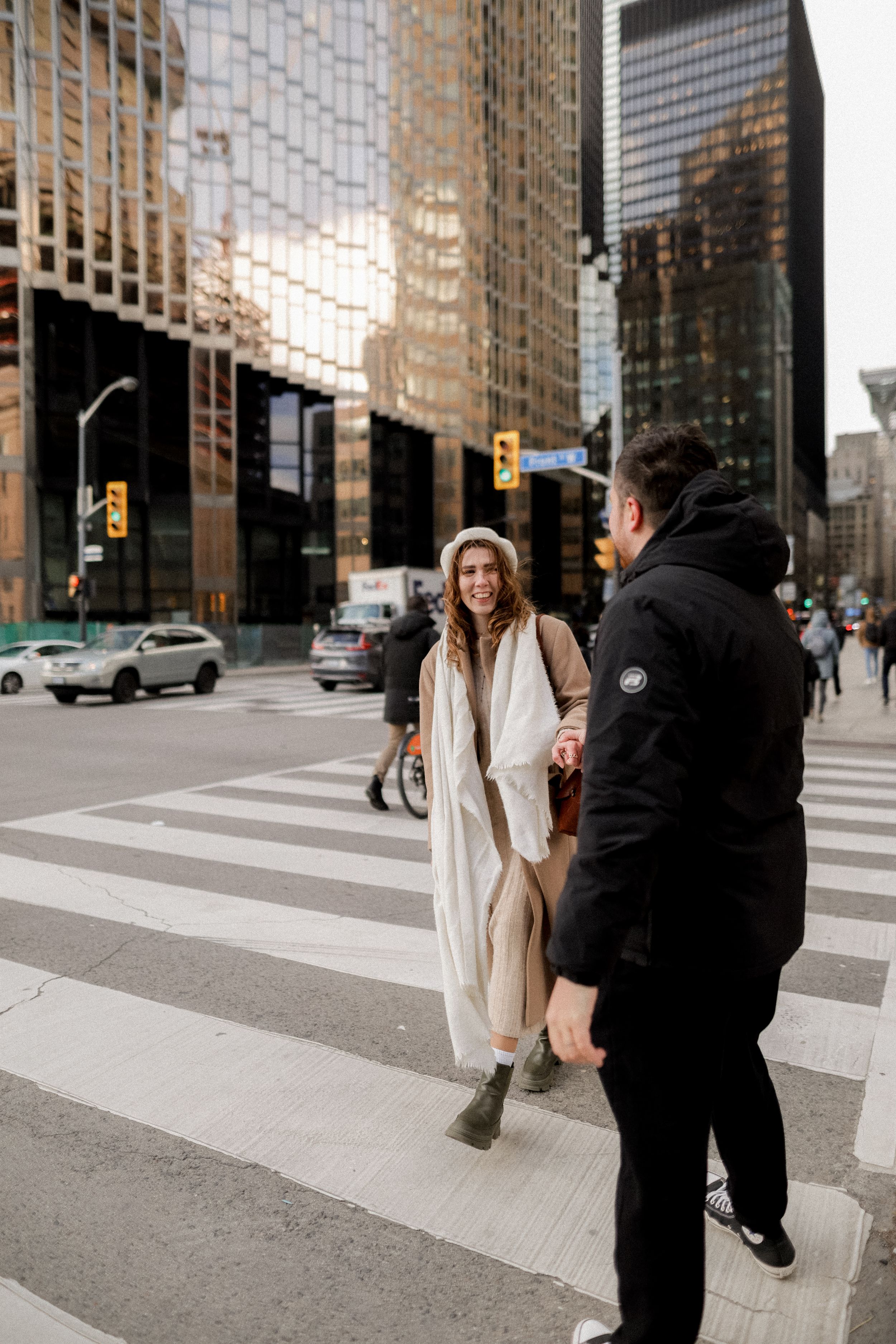 Two people interacting on a crosswalk with modern glass buildings reflecting sunlight in the background.