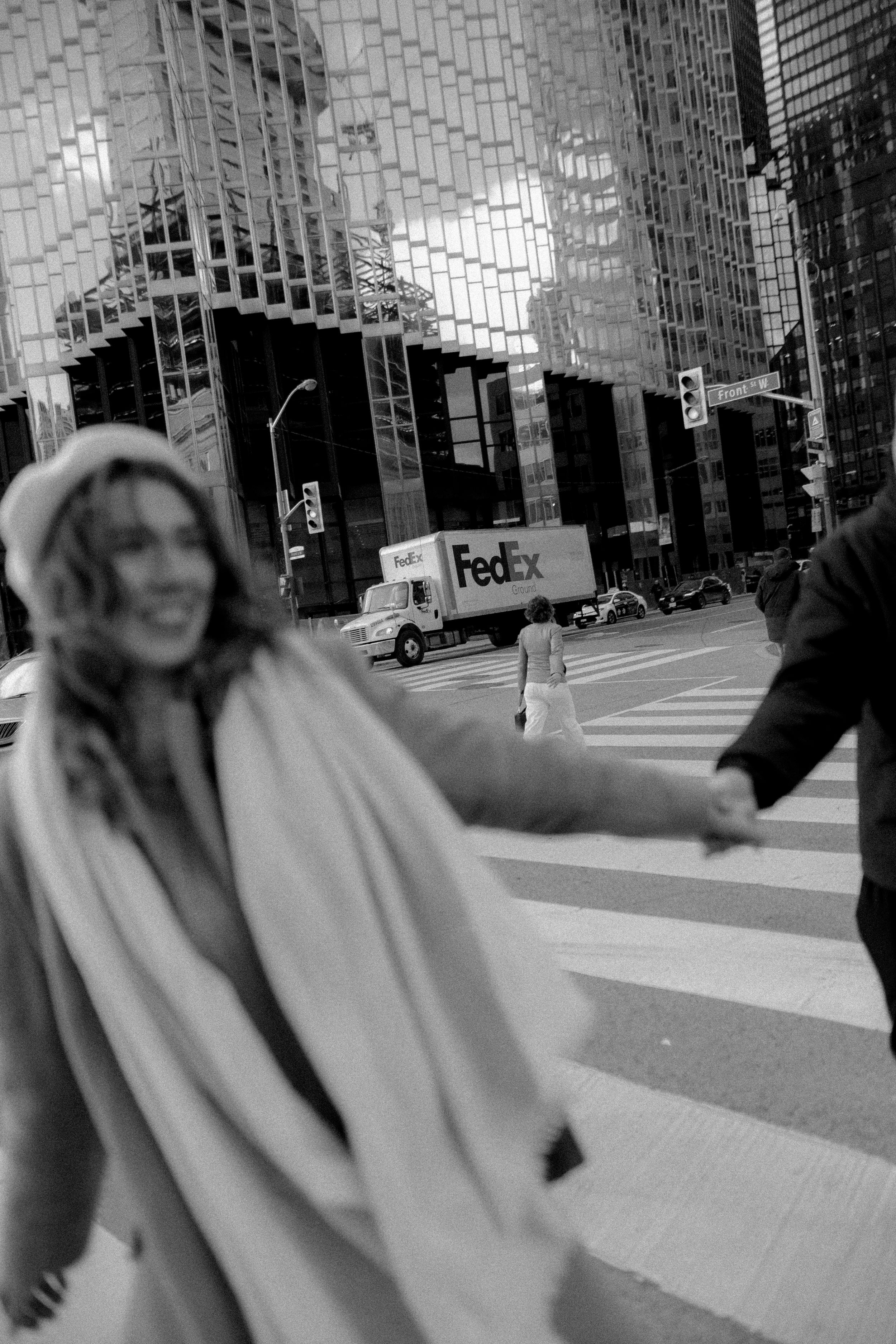 A black and white street scene with people crossing an intersection near a FedEx truck in the city.