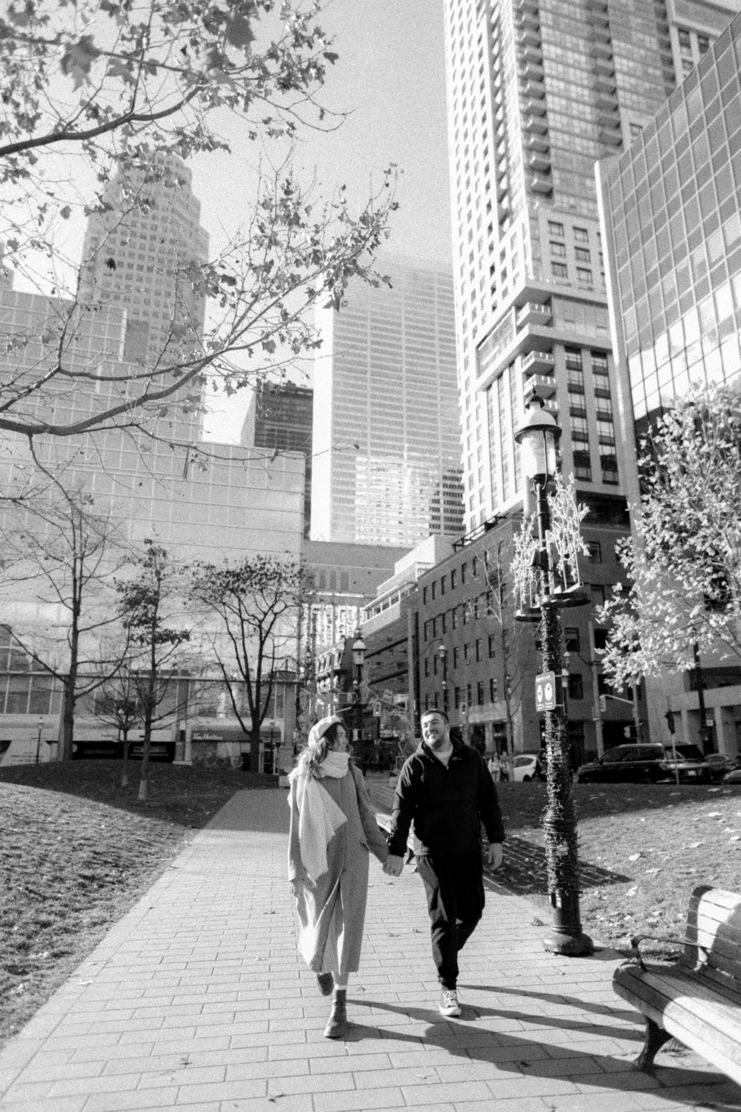A couple strolling down an urban pathway with tall skyscrapers in black and white.